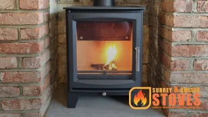 A modern black wood burning stove with a lit fire, installed in a brick-lined fireplace recess, by Surrey & Sussex Stoves.