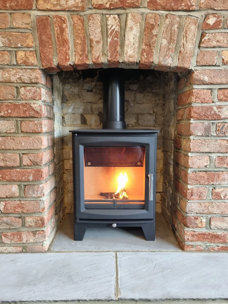 Alt Text: Completed wood burning stove installation with a lit fire in a restored Worthing fireplace by Surrey and Sussex Stoves.