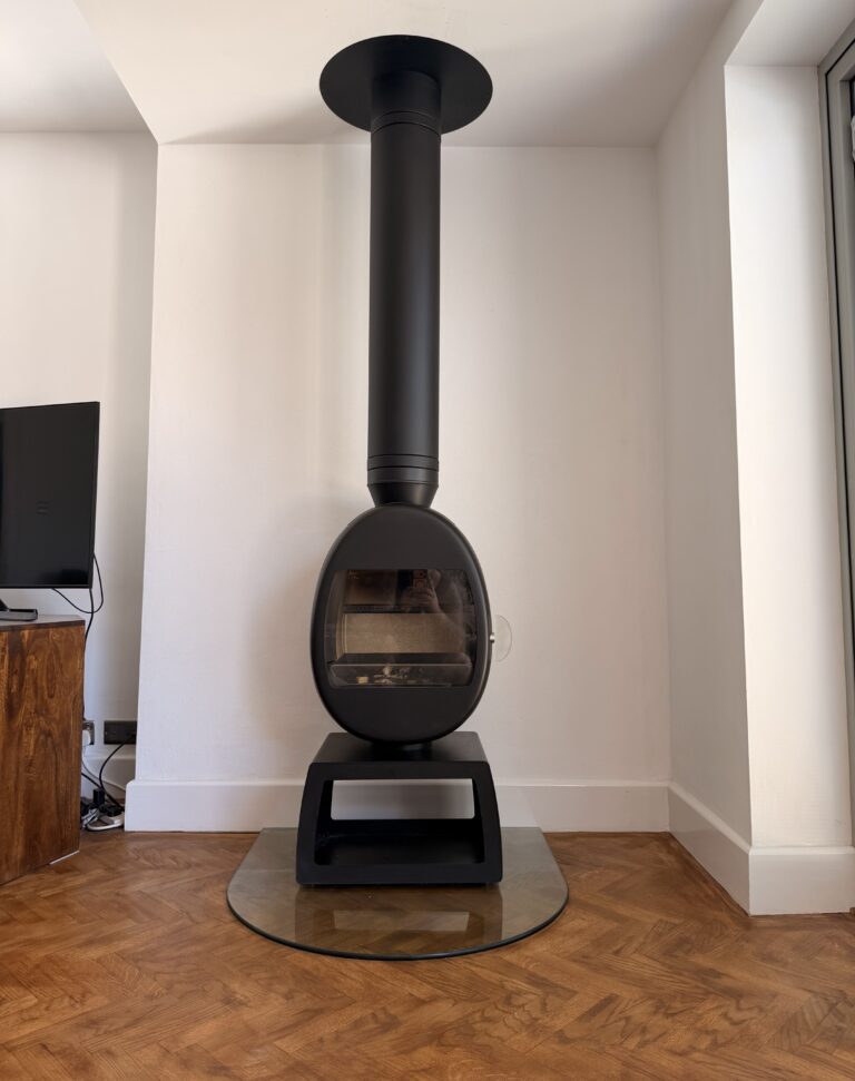 Contemporary egg-shaped wood burning stove installed with a straight ceiling flue and glass hearth in East Preston, West Sussex, by Surrey and Sussex Stoves. HETAS registered installation.