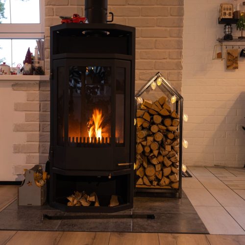 Black metal stove fireplace with wood in a woodpile - the interior of a private village house. Heating and heating of the house with firewood, the heat of the fire from the hearth.