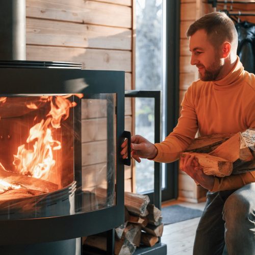 Man is putting wood into the fireplace indoors in the house.