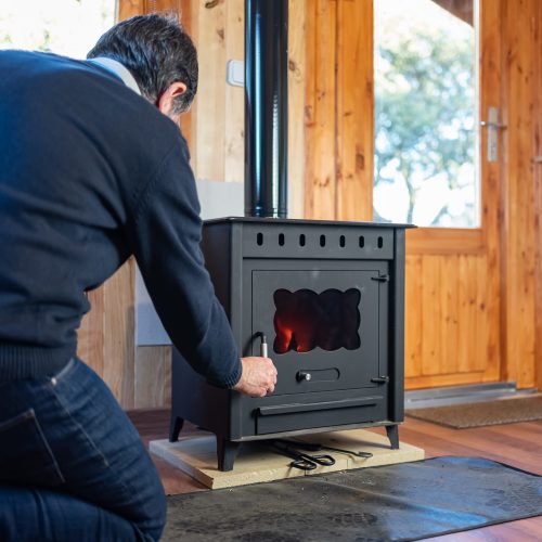 Man opening the door of a rustic cast iron stove to light the fire